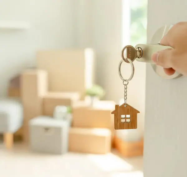 Front door opening with house-shaped keyring and moving boxes inside, symbolising buying or selling a home in Scotland
