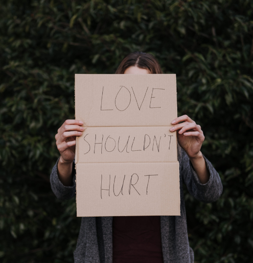 A woman holding a cardboard sign reading "Love shouldn’t hurt" to raise awareness of domestic abuse.