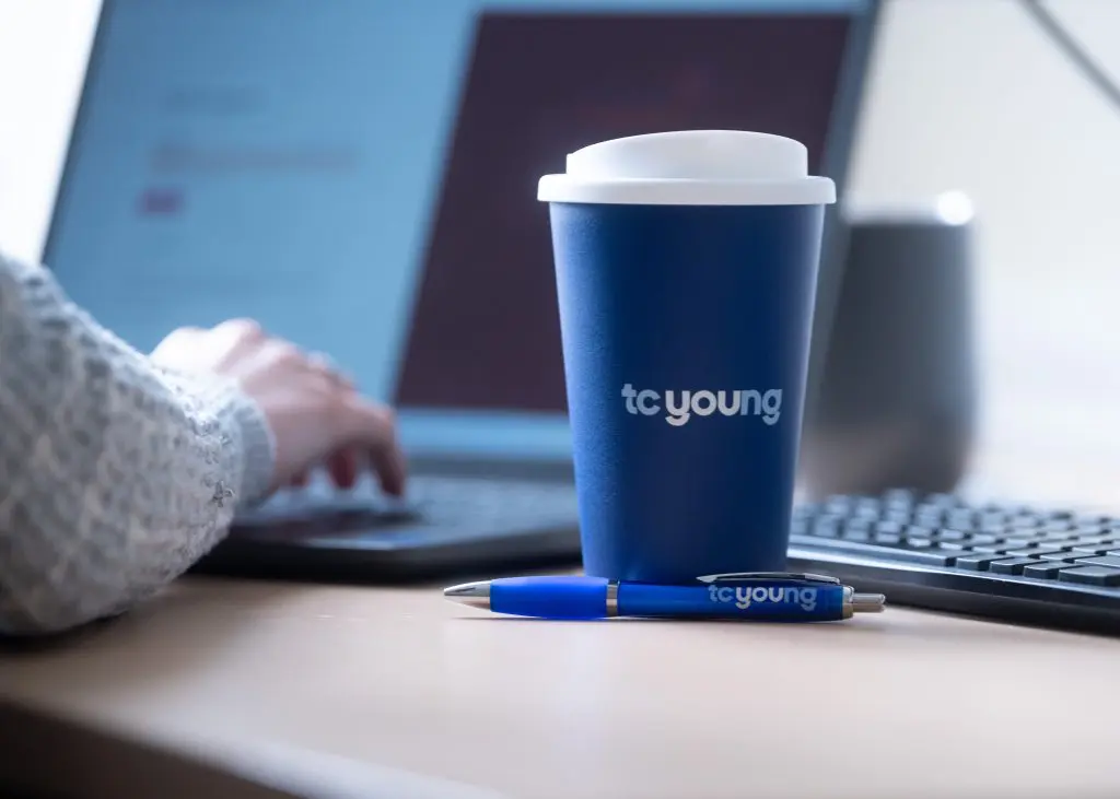 Solicitor typing case notes on will dispute with TC Young coffee cup and pen"