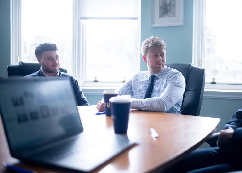 TC Young solicitors around a table with an open laptop, discussing contract disputes in Scotland