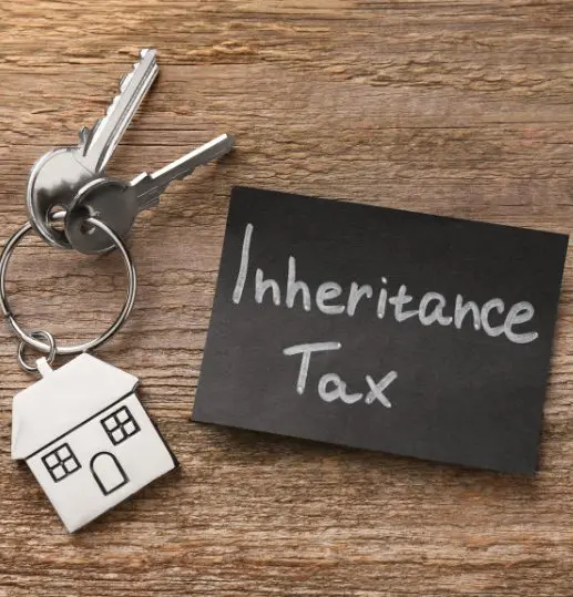 House keys with a house-shaped keyring next to the words “inheritance tax” on a slate surface