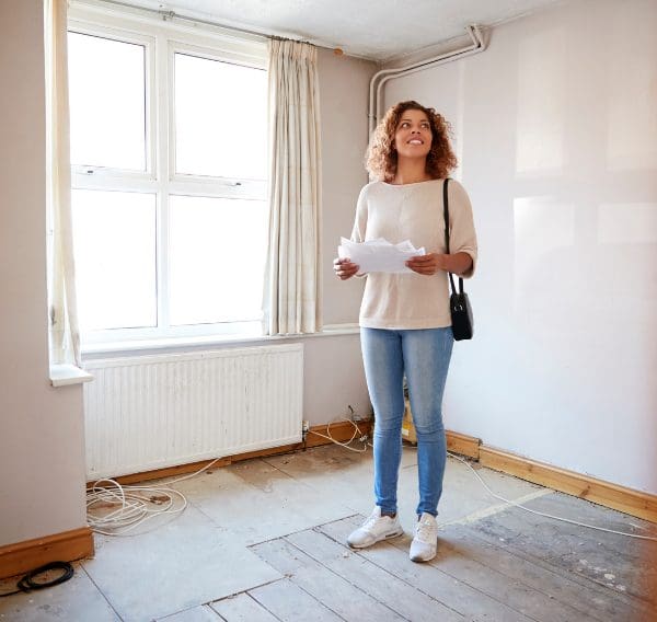 First-time buyer standing in renovation property with house plans, representing buying your first home in Scotland