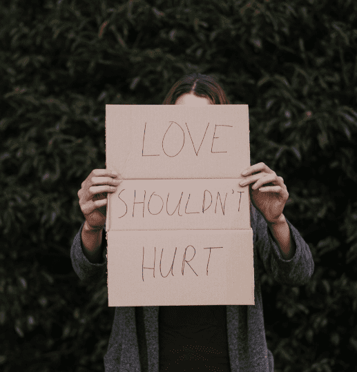 A woman holding a cardboard sign reading "Love shouldn’t hurt" to raise awareness of domestic abuse.