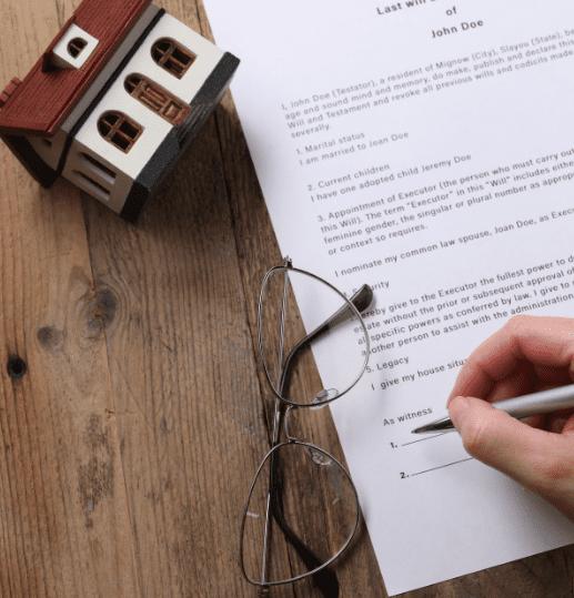 Person signing a disputed will with spectacles and miniature house nearby