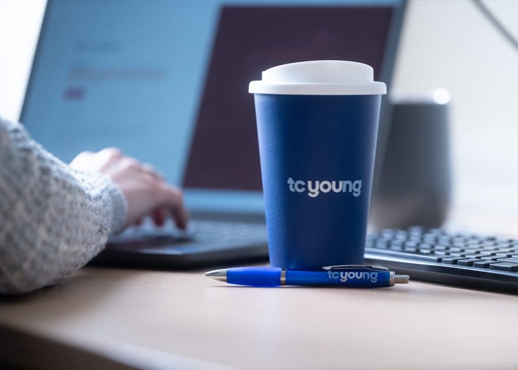 Solicitor typing case notes on will dispute with TC Young coffee cup and pen"