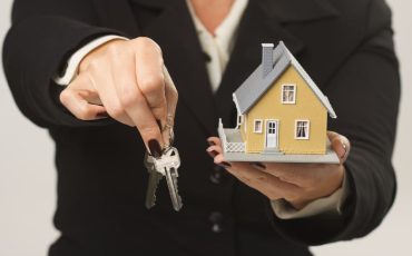 Female presenting keys and small house.