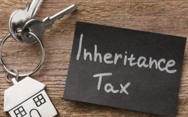 House keys with a house-shaped keyring next to the words “inheritance tax” on a slate surface